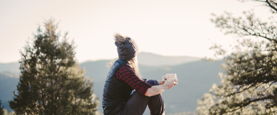 Body and Soul - woman sitting on blanket on a rock with cup in her hand as she gazes across the valley | Nashville Christian Family Magazine